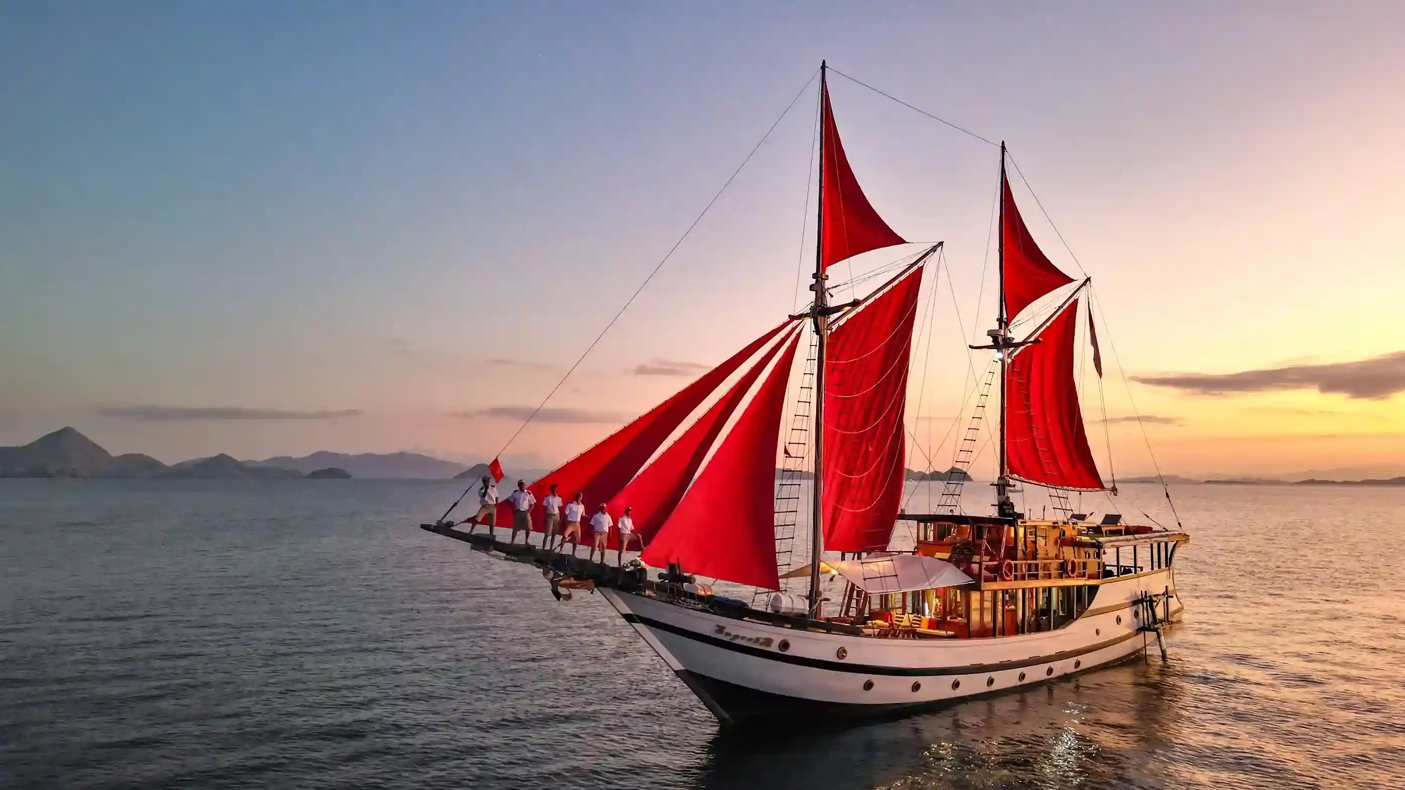 Red-sailed phinisi under sail at dusk