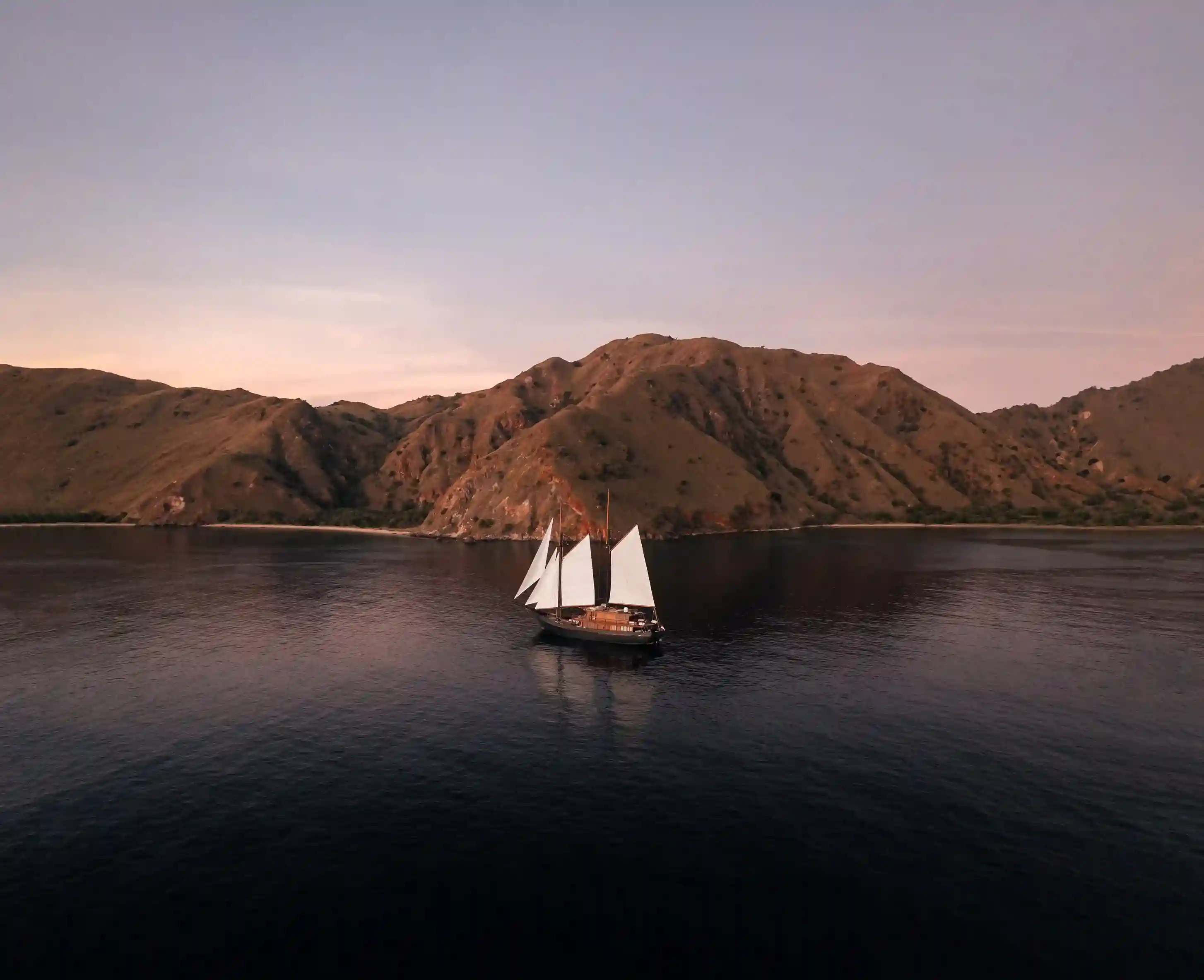 Small phinisi at anchor under an island ridge